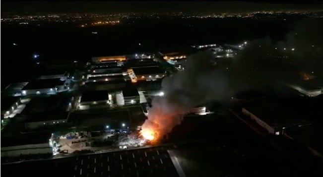 Deposito di rifiuti ferrosi in fiamme, fumo nero e aria irrespirabile